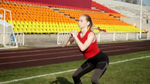 Joven delgado caucásico rubio hembra en ropa deportiva hace ejercicios deportivos en el estadio — Vídeos de Stock