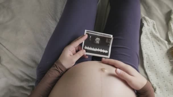 Expecting pregnant woman with large belly looking at ultrasound scan at home — Stock Video