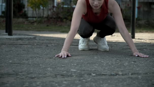 Young female in activewear sitting, holding hands on ground in plank position — Stock Video