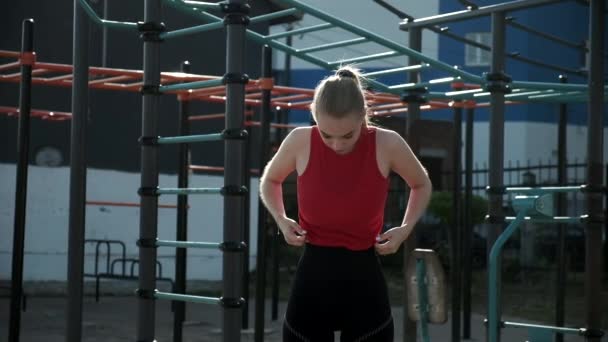 Молодая грудастая женщина с хвостиком стоит на спортивной площадке, стягивает штаны. — стоковое видео