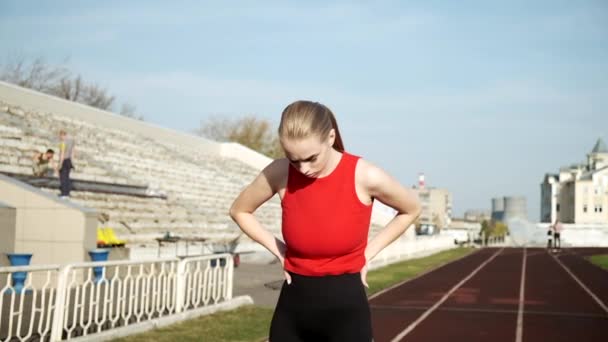 Сфокусированный грудастый бегун в спортивной одежде, стоящий на стадионной дорожке в солнечный день — стоковое видео