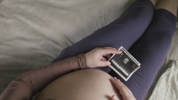 Αναμένοντας έγκυο γυναίκα με μεγάλη κοιλιά κοιτάζοντας υπερηχογράφημα στο σπίτι — Αρχείο Βίντεο