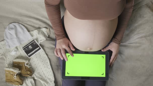 妊娠中の女性を期待します大きな腹ベッドの上にクロマキーとタブレットを使用して — ストック動画