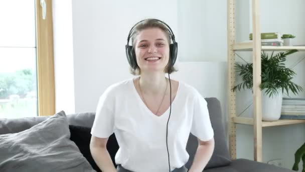 Cabelo curto jovem caucasiano sorrindo mulher tira fones de ouvido em casa. — Vídeo de Stock