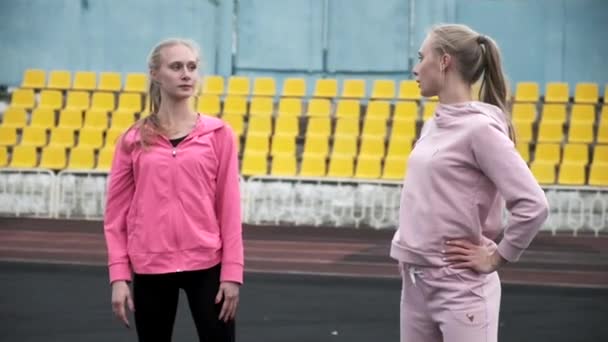 Młode białe bliźniaki w sportowej odzieży uśmiechnięte i mówiące na stadionie — Wideo stockowe