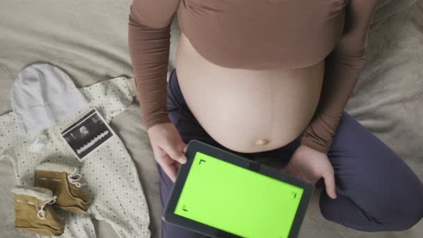 Očekává těhotnou ženu s velkým břichem pomocí tablety s chromakey na posteli — Stock video
