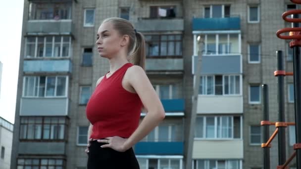 Jeune femme blonde aux gros seins avec queue de cheval en haut rouge expire au terrain de sport — Video