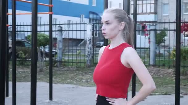 Jeune femme blonde aux gros seins avec queue de cheval en haut rouge se tient au terrain de sport — Video