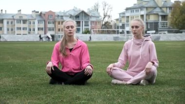 Pembe spor giyimli iki genç ikiz Lotus pozisyonunda çimlerde oturur, meditasyon yaparlar.