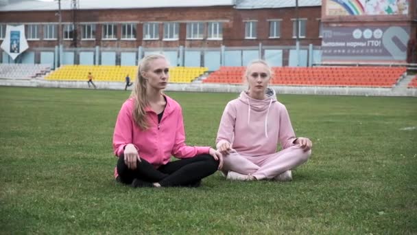 Dos jóvenes gemelos concentrados en ropa deportiva comienzan a meditar al aire libre — Vídeos de Stock