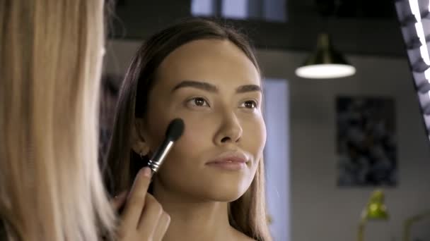 Maquillaje artista haciendo maquillaje para morena mujer asiática con cepillo en salón de belleza — Vídeos de Stock