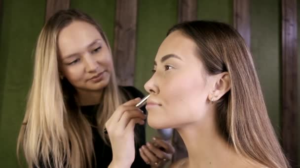 Atractivo caucásico maquillaje artista haciendo maquillaje para asiático femenino en salón de belleza — Vídeos de Stock