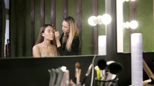 Maquillaje artista haciendo maquillaje para chica asiática en salón de belleza, reflexión en espejo — Vídeos de Stock