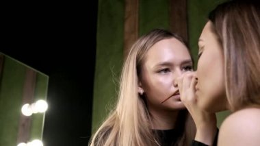 Çekici beyaz makyaj sanatçısı güzellik salonunda genç bir bayan için makyaj yapıyor.