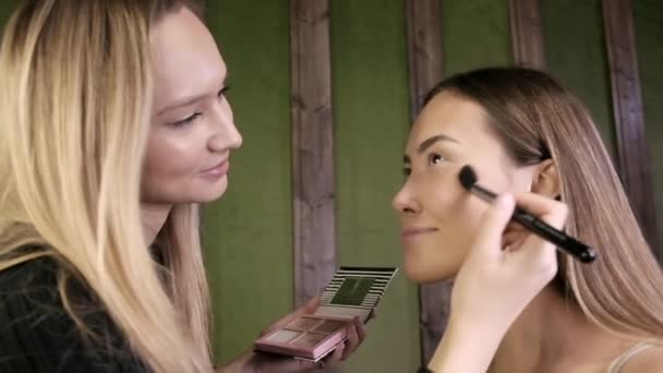 Atractivo caucásico maquillaje artista haciendo maquillaje para asiático femenino en salón de belleza — Vídeo de stock