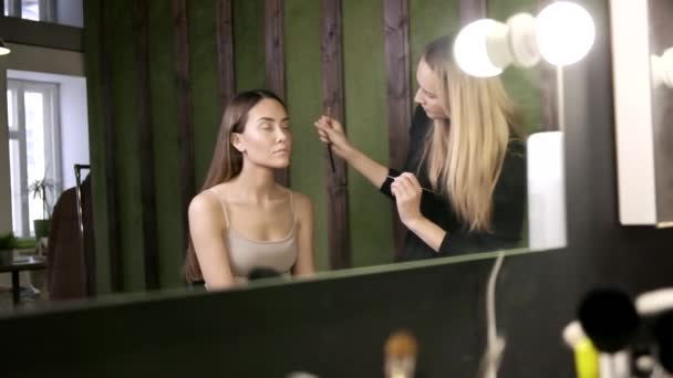 Maquillage artiste faire maquillage pour asiatique fille dans salon de beauté, reflet dans miroir — Video