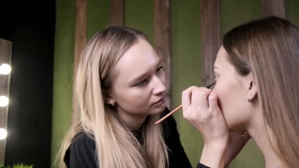 Привлекательная кавказская визажистка делает макияж для азиатки в салоне красоты — стоковое видео
