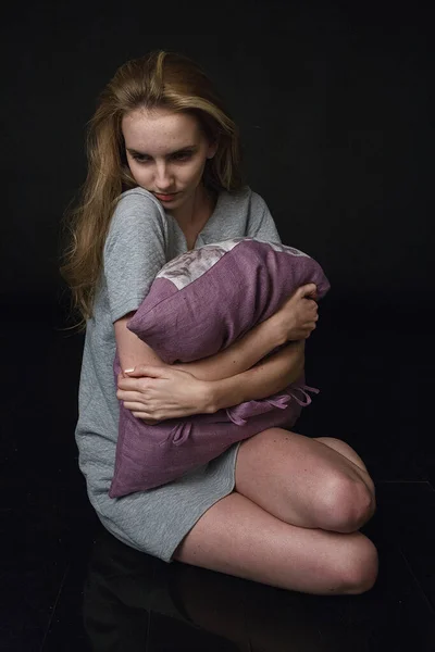 Joven bastante caucásico flaco mujer en vestido gris se sienta en el suelo, abraza la almohada — Foto de Stock
