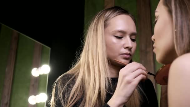 Vonzó kaukázusi smink művész csinál smink fiatal nő szépségszalonban — Stock videók