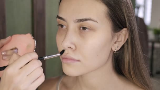 Make up artist doing makeup for brunette asian woman with brush in beauty salon — Stok Video