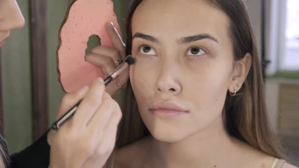 Maquillaje artista haciendo maquillaje para morena mujer asiática con cepillo en salón de belleza — Vídeos de Stock
