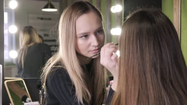 Atractivo caucásico maquillaje artista haciendo maquillaje para asiático chica en salón de belleza — Vídeo de stock