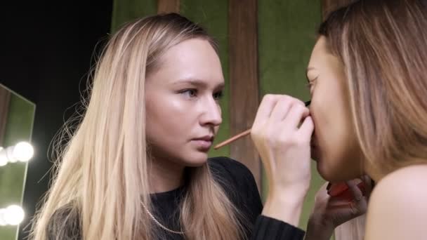 Atractivo caucásico maquillaje artista haciendo maquillaje para asiático femenino en salón de belleza — Vídeo de stock