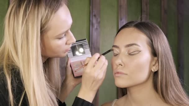 Atraente caucasiano maquiagem artista fazendo maquiagem para asiático feminino no salão de beleza — Vídeo de Stock