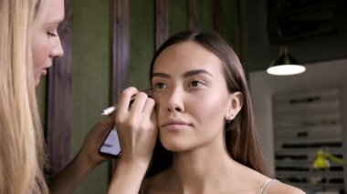 Makyöz, güzellik salonunda göz kalemi olan Asyalı bir kadın için makyaj yapıyor.