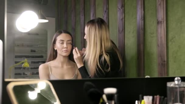 Make up artist doing makeup for asian girl in beauty salon, reflection in mirror — Stock Video