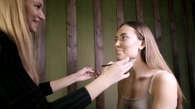 Çekici beyaz makyaj sanatçısı Asyalı bir kadın için güzellik salonunda makyaj yapıyor.