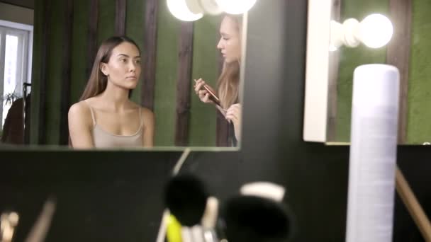 Maquillage artiste faire maquillage pour asiatique fille dans salon de beauté, reflet dans miroir — Video