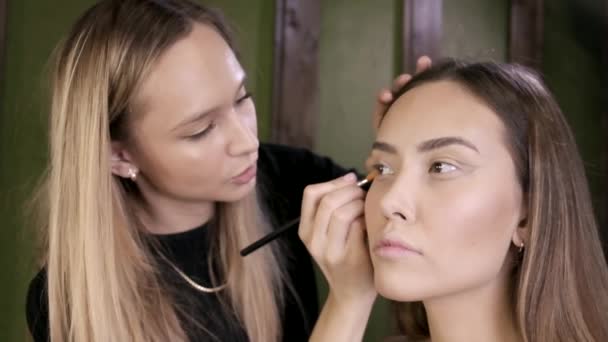 Atraente caucasiano maquiagem artista fazendo maquiagem para asiático feminino no salão de beleza — Vídeo de Stock