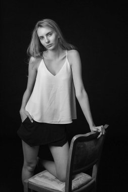 Uzun saçlı, siyah arka planda, sandalyede oturan genç ve güzel bir kadın.