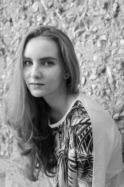 Beyaz tenli, doğal çekici kadın model taş duvarın önünde duruyor.