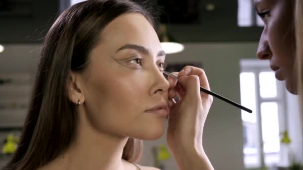 Maquillaje artista haciendo maquillaje para morena mujer asiática con cepillo en salón de belleza — Vídeo de stock