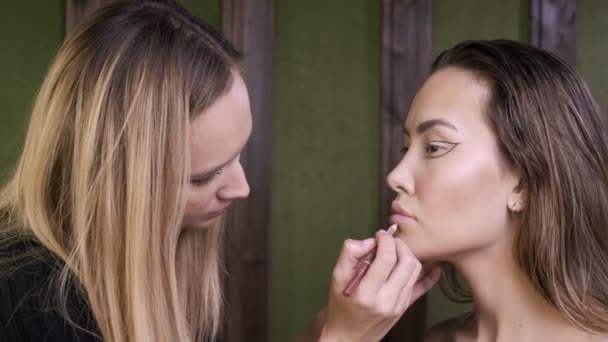 Professionele make-up kunstenaar schilderen lippen van jonge brunette aziatische vrouw op salon — Stockvideo