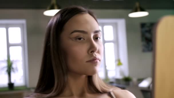 Ung brunett söt kvinna med kreativ makeup tittar på spegel på salongen — Stockvideo