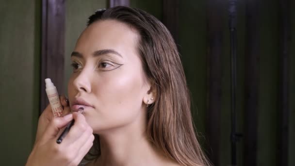 Makeup artist ζωγραφική χείλη της νεαρής ασιάτισσας όμορφη γυναίκα με πινέλο στο σαλόνι — Αρχείο Βίντεο