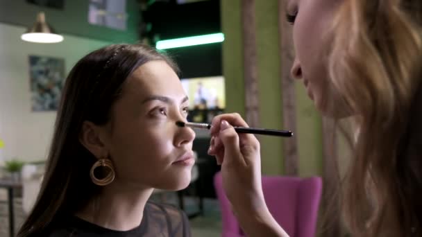 메이크업 아티스트는 미용실에서 솔을 사용하여 여자 얼굴에 기본 톤 크림을 바르고 있다 — 비디오