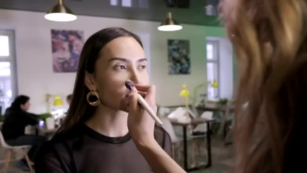 Makyaj sanatçısı güzellik salonunda fırça kullanarak kızların yüzüne temel ton kremi sürüyor. — Stok video
