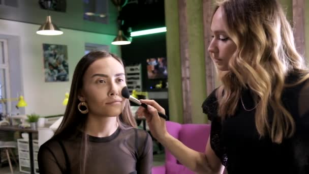Artista de maquillaje haciendo maquillaje para atractivo joven asiático hembra en salón de belleza — Vídeo de stock