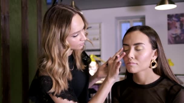Maquiagem artista fazendo maquiagem para atraente jovem asiático feminino no salão de beleza — Vídeo de Stock