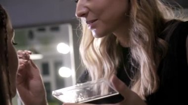 Makyaj sanatçısı güzellik salonundaki çekici esmer kızın makyajını yapıyor.