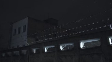 Soğuk, karanlık kış gecesinde, kar yağarken beton çitin üzerinden dikenli teller örülmüş.
