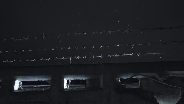 Soğuk, karanlık kış gecesinde, kar yağarken beton çitin üzerinden dikenli teller örülmüş. — Stok video