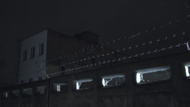 Prison barbelé fil sur clôture en béton à froid nuit d'hiver sombre pendant les chutes de neige — Video