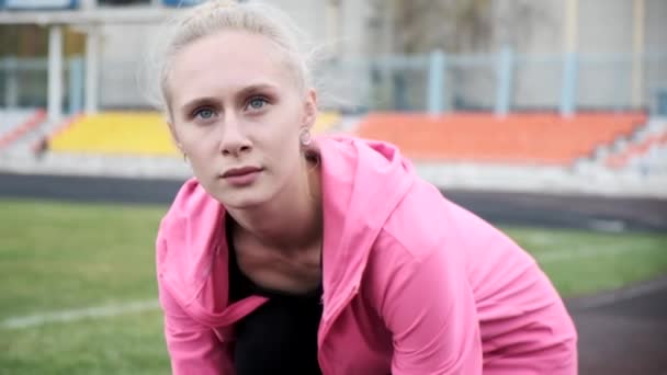 Jonge blanke vrouw in roze hoodie zittend op de grond in het stadion, close-up — Stockvideo