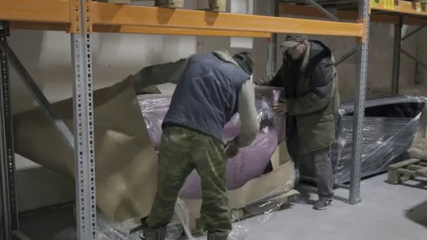 РОССИЯ, Владимир, 30 МАР 2021: двое мужчин-перевозчиков передвигают упакованный диван на складе — стоковое видео