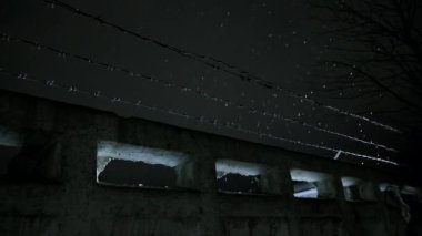 Soğuk, karanlık kış gecesinde, kar yağarken beton çitin üzerinden dikenli teller örülmüş.
